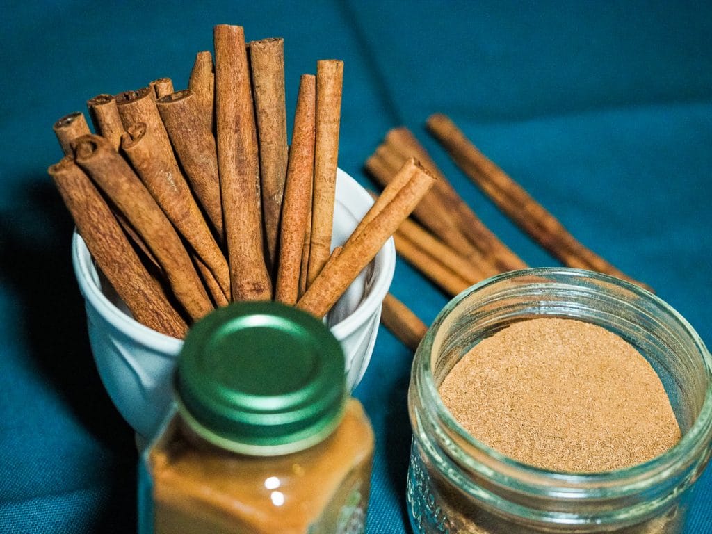 Cinnamon stick on a white small cup, cinnamon powder in a glass container and another cinnamon powder in a small jar with green lid.