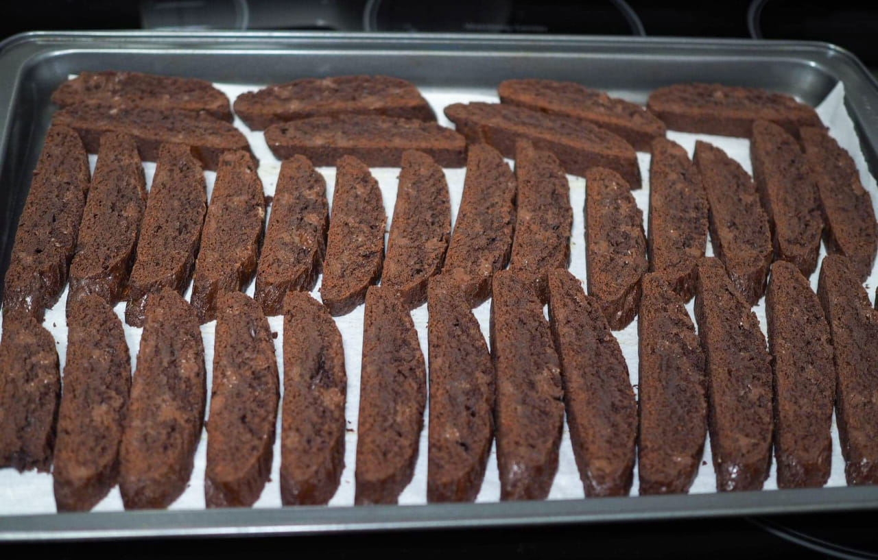 Chocolate biscotti arranged cut-side down on a lined cookie baking sheet