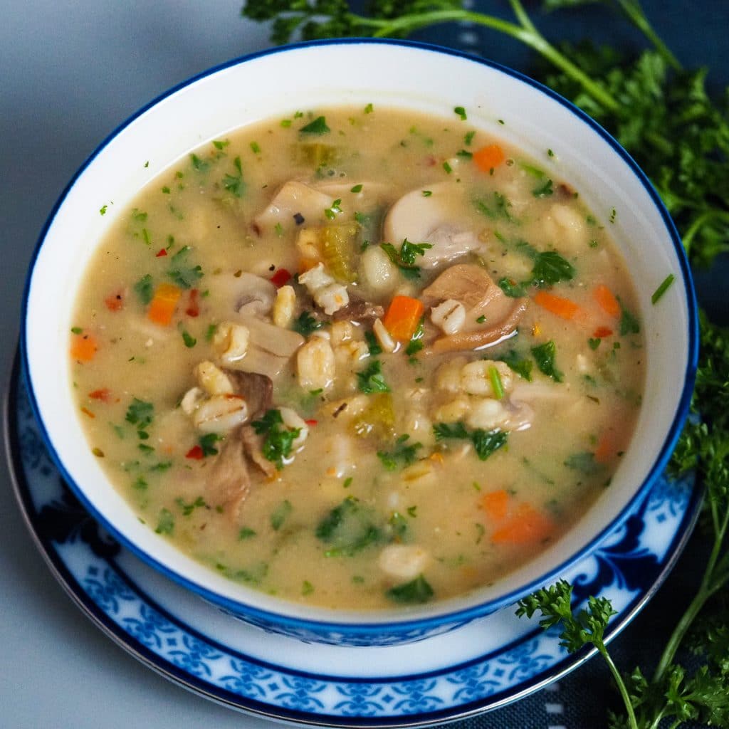 Oatmel blend soup with chopped carrots, sliced mushrooms and parsley in a white and blue bowl .