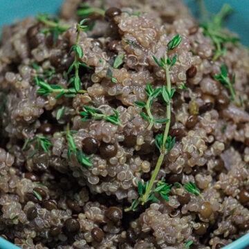 Cooked quinoa and black lentils in a turquoise bowl garnished with fresh thyme.
