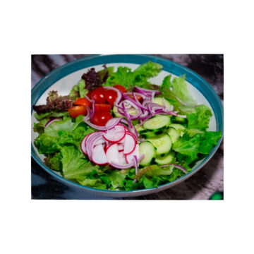 A big bowl of mixed chopped lettuce, sliced red radish, sliced cucumber,Sliced cherry tomatoes and thinly sliced red onion with lemon and ginger vinaigrette on a large blue and white serving bowl.