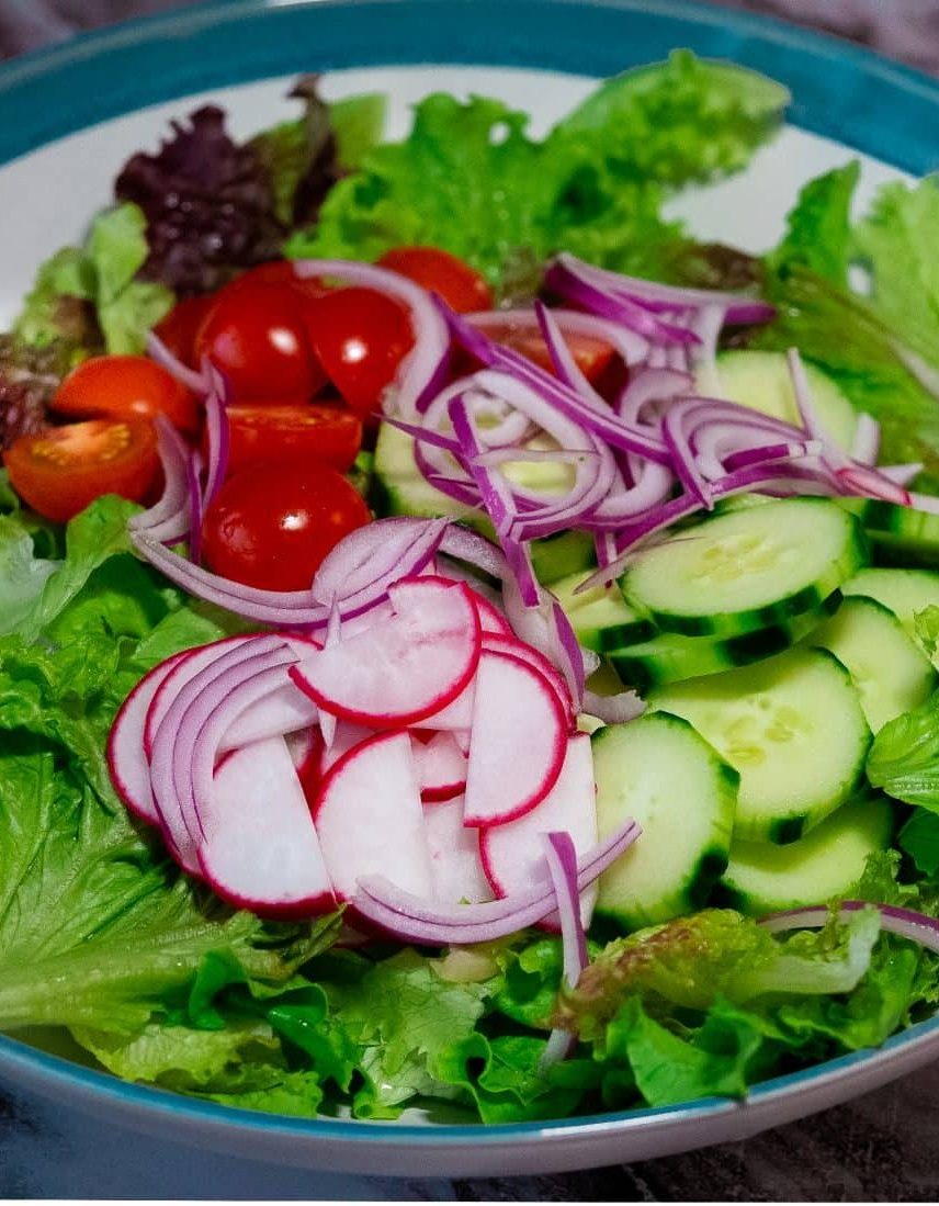A big bowl of mixed chopped lettuce, sliced red radish, sliced cucumber,Sliced cherry tomatoes and thinly sliced red onion with lemon and ginger vinaigrette on a large blue and white serving bowl.