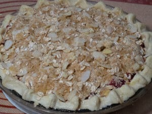 Raw pie dough on a baking dish filled with strawberry-rhubarb filling topped with almond and oat streusel toppings