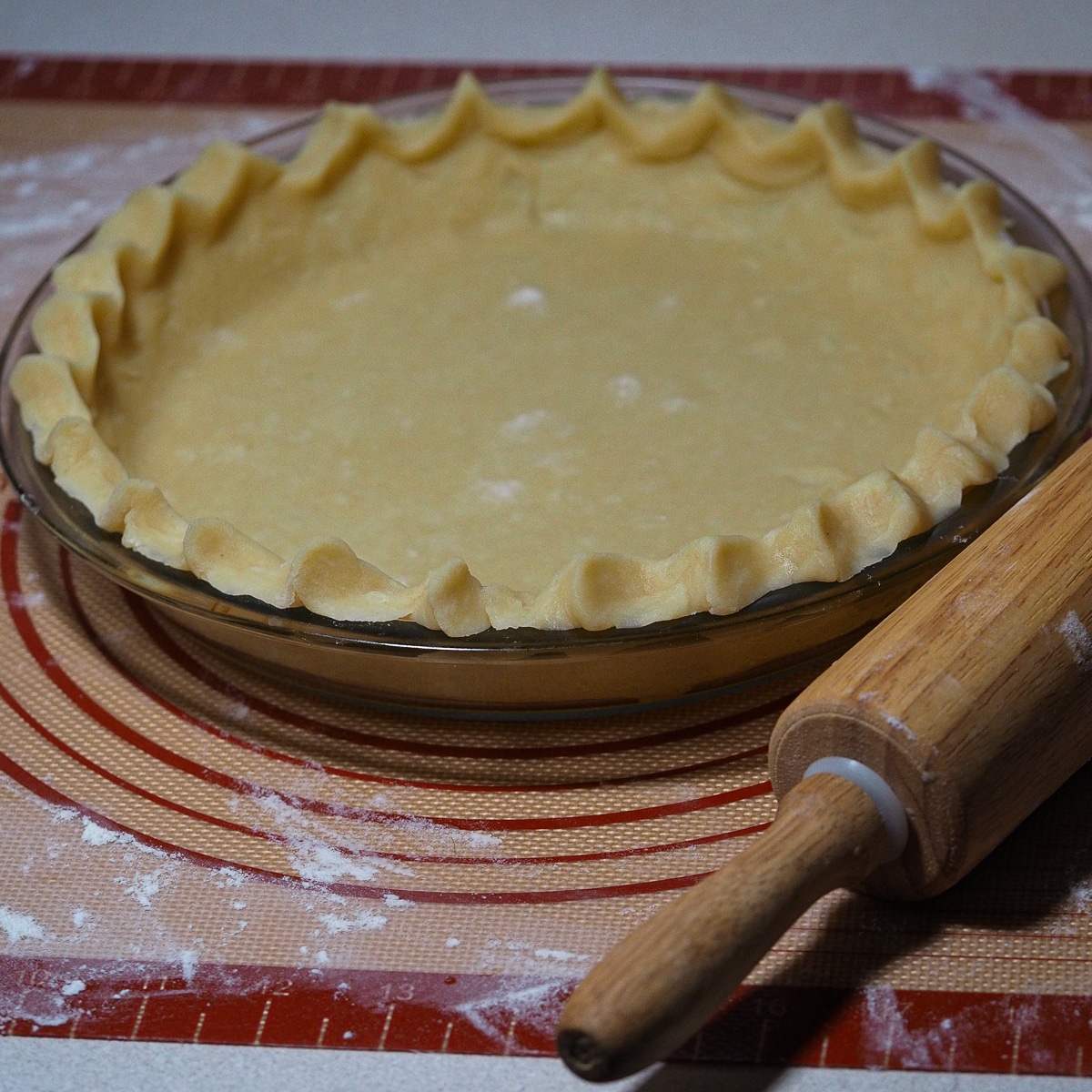 Pie dough on a glass pie dish with wooden rolling pin on the side.