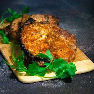 Nice browned pork chops on a bamboo board placed on top of a cement working space adorned with green cilantro