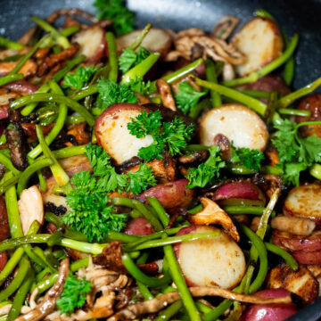 Sliced red potatoes, Chopped garlic scapes, mixed mushrooms stirfry in a sautee pan garnished with parsley leaves.