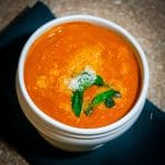 Tomato soup in a white bowl top with grated parmesan cheese and garnished with basil leaf.