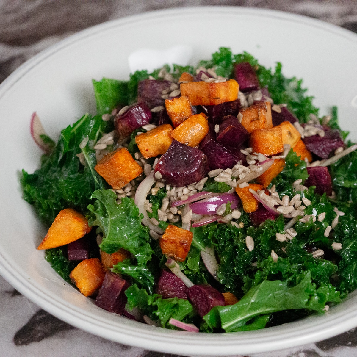 Chopped kale, sweet potatoes, red onion and sunflower seeds salad in a white bowl