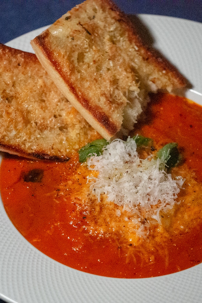 Tomato soup in a white bowl, with grated cheese and toasted garlic-parmesan bread