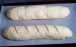 2 long loaf bread dough , one with slashes on top placed in a baking sheet lined with parchment paper.