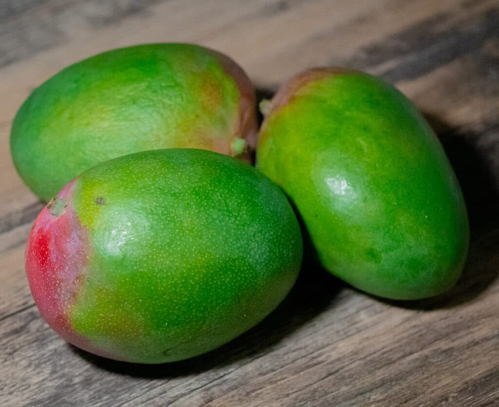 Three green mango on a wooden surface