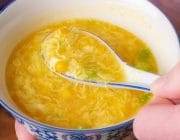 The best corn and egg drop soup on a blue rimmed bowl with Chinese spoon