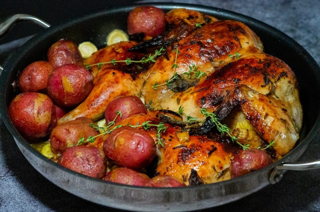 Spatchcock roasted chicken and red baby potatoes in a large non-stick pan garnished with fresh thyme.