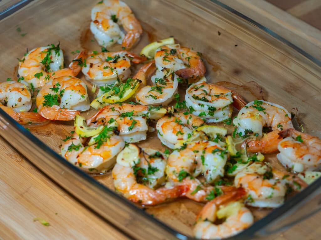 15 minutes lemon-garlic shrimp with chopped parsley in a glass baking on top of a wooden board .