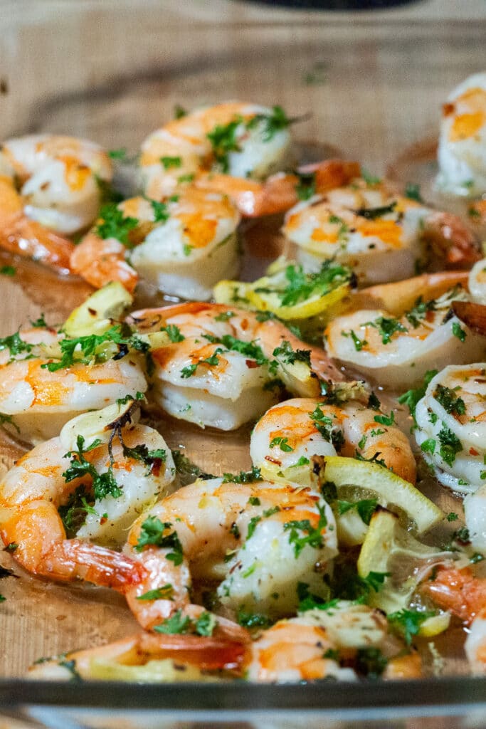 baked shrimp with thinly sliced lemon, chopped parsley and lemon zest in a glass baking dish.