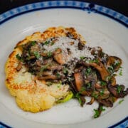 Seared cauliflower steak top with sauted mushrooms garnished with chopped parsley and grated parmesan cheese