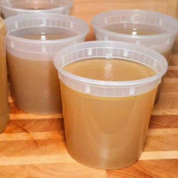 Homemade chicken stock in a plastic container placed on top of the wooden board