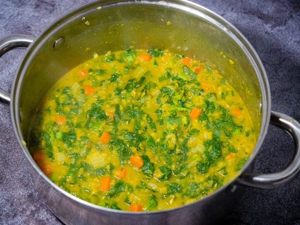 Cooked curried split peas and kale in the sauce pan laced on top of the dark grey counter top.