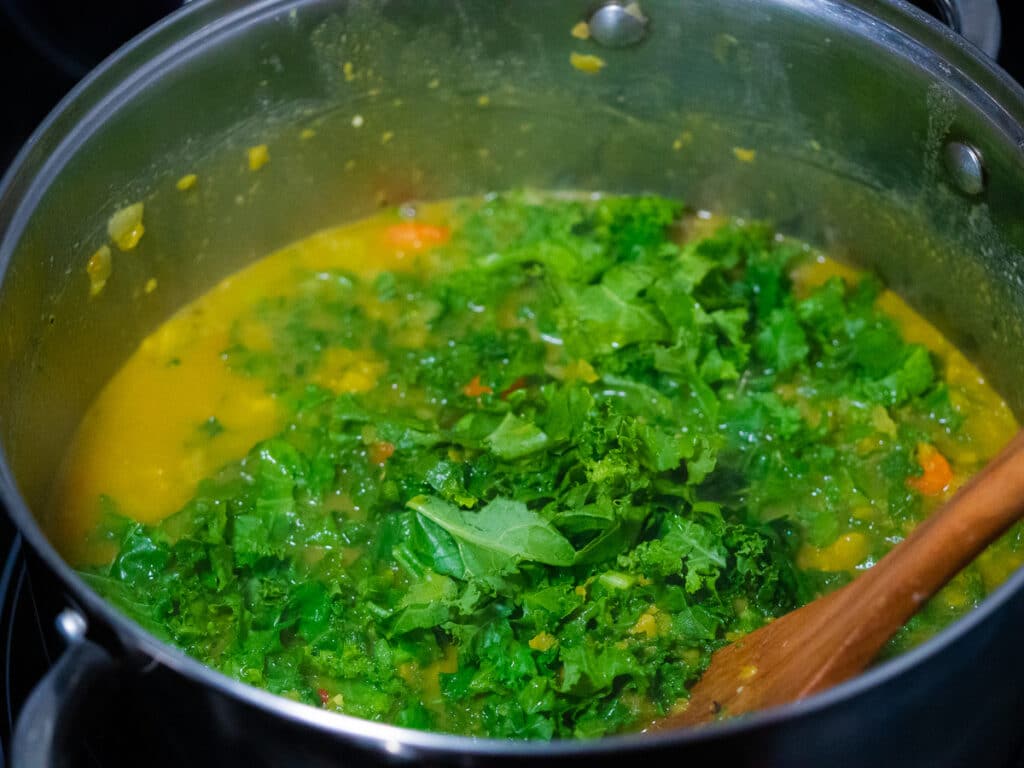 Mixing kale into the curried peas cooking liquid in a sauce pan