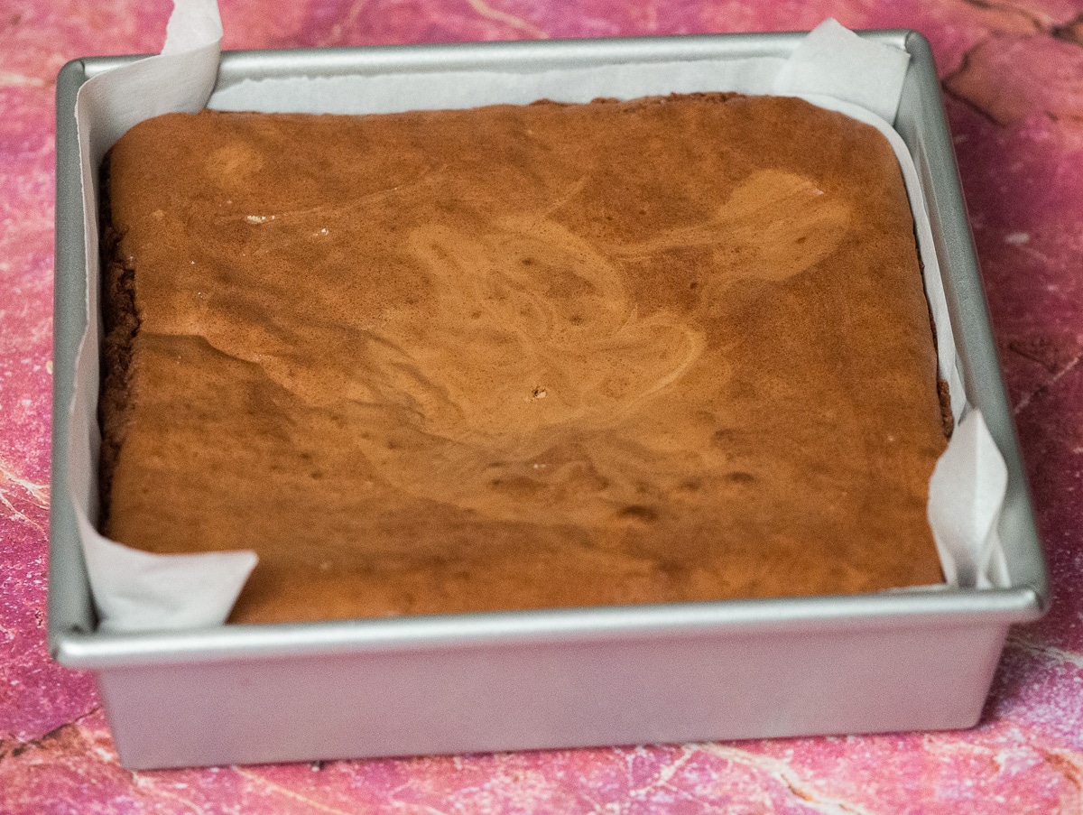 Baked brownie in the pan on top of pink counter top.