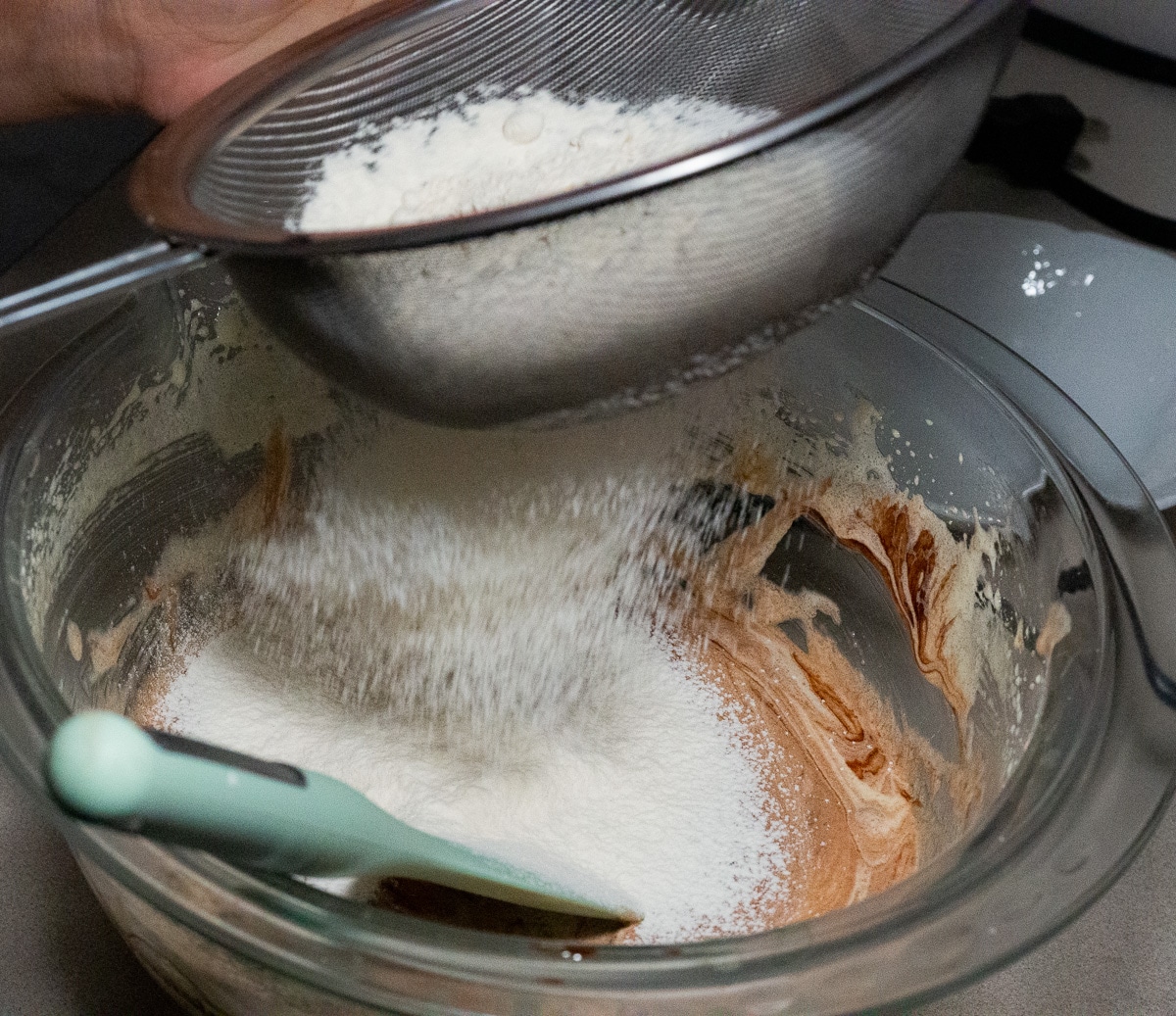 Sifting flour into the eggs mixture in a glass mixing bowl.
