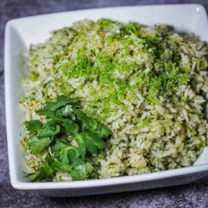 Cooked herby rice on a square bowl garnished with lime zest and Ccilantro