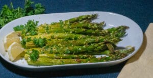 Roasted asparagus placed in a white serving dish with chopped parsley and lemon zest placed on top
