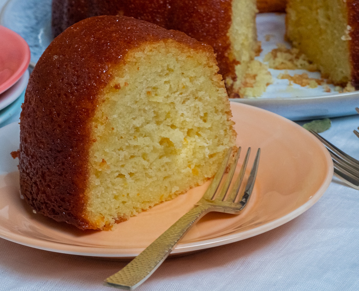 A slice of spiced orange and lemon pound cake placed in orange cake plate with gold dessert fork at the side.