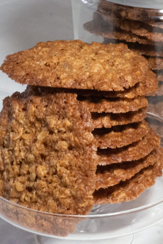 Stacks of thin and crispy oatmeal cookies on a glass serving dish.