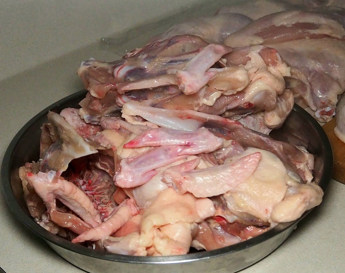 Chicken bones in a stainless steel container and chicken pieces behind