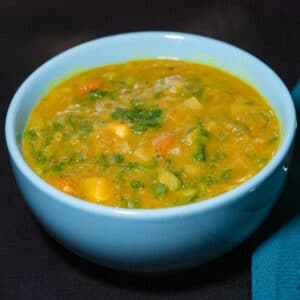 Curried split peas soup with chopped kale, diced carrots and dice onion in a turquoise soup bowl on a black surface with dark green linen on the side
