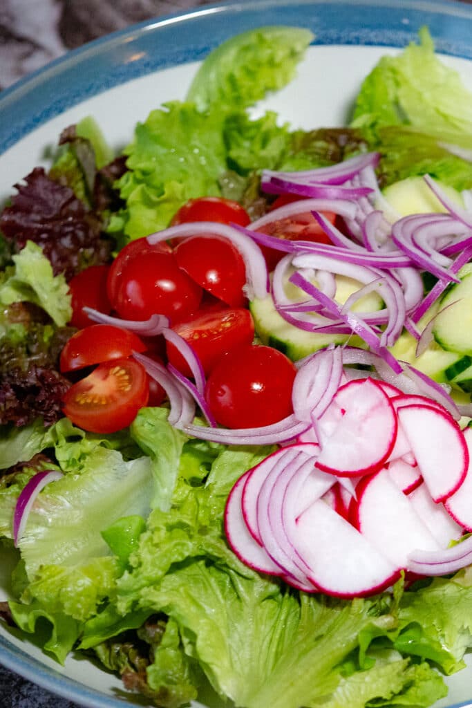 Chopped crisp oakleaf lettuce, sliced raddish, cherry tomatoes,cucumber and red onion on a salad serving bowl.