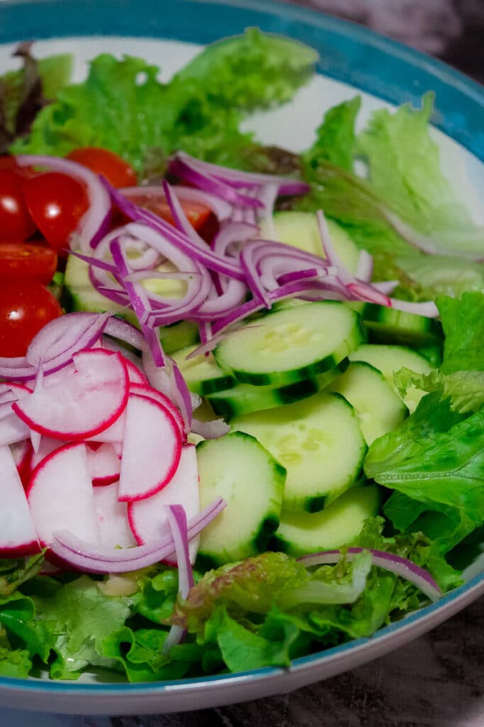 Chopped crisp lettuce, sliced cucumber,raddish, cherry tomatoes and red onion in a blue and white salad bowl