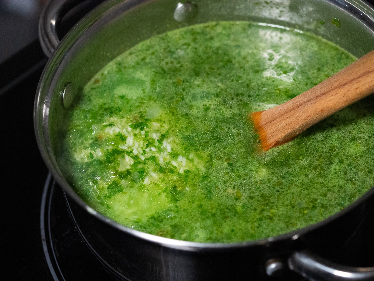 Rice and green cooking liquid in a stainless steel sauce pan with wooden spoon for stirring.