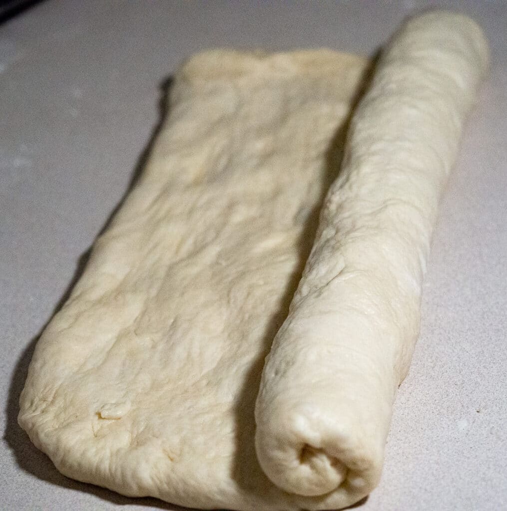 Rolling bread dough for long long loaf bread on a white counter top