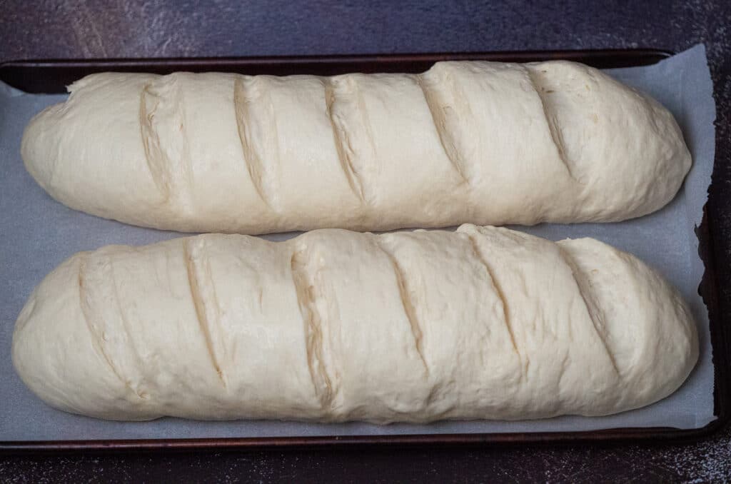 Two risen long long bread dough placed in a lined baking sheet