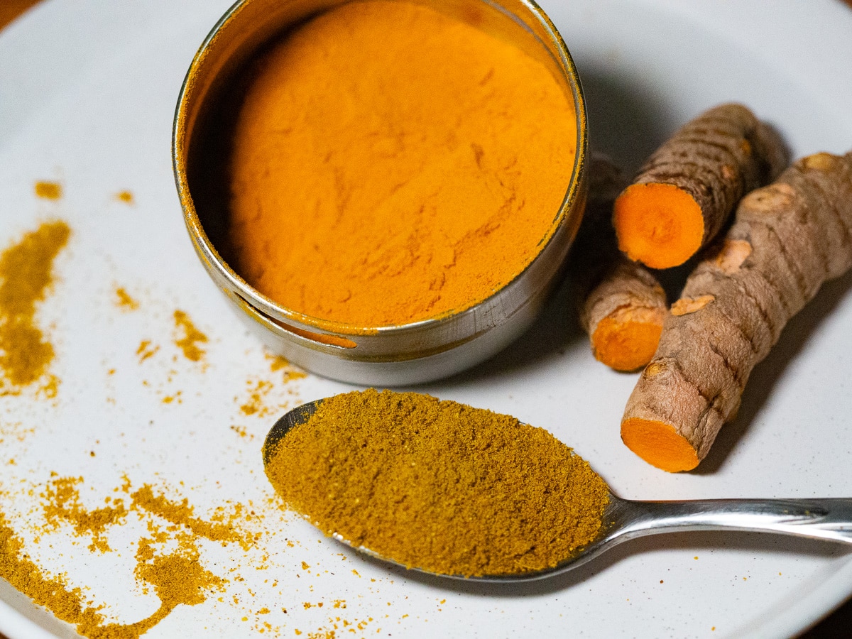 Turmeric powder in a tin, turmeric roots and curry powder in a silver spoon