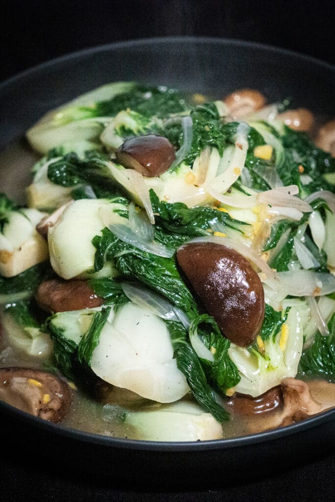 Bok choy and shitaki mushroom recipe with sauce in a black serving bowl