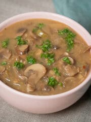 Mushroom soup in a pink bowl garnished with parsley and a green linen on the side.