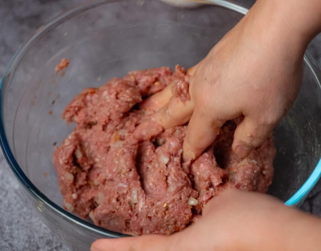 mixing meatballs by hand in a glass mixing bowl