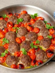 Beef meatballs and blistered cherry tomatoes in a pan on a beige linen covered tables