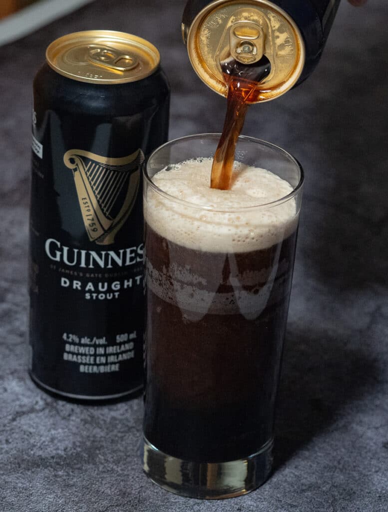 A bottle of guinness beer in a can and one pouting in a glass.