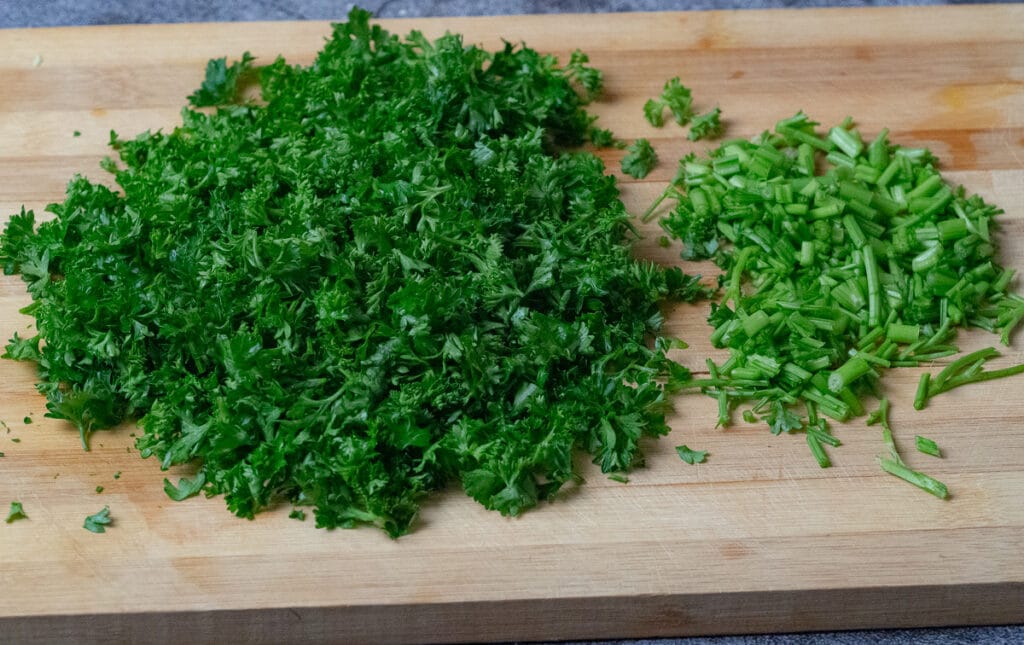 Chopped parsley, leaves and stem separated placed on a wooden board.