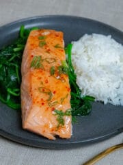 Baked sweet chilli salmon on a bed of sauteed spinach and steamed rice in a black plate