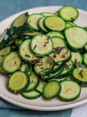 Sautéed zucchini with garlic and oregano in a white dish placed on top og green and white surface