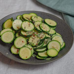Sauteed zucchini with garlic and oregano in a black serving plate on a grey linen covered