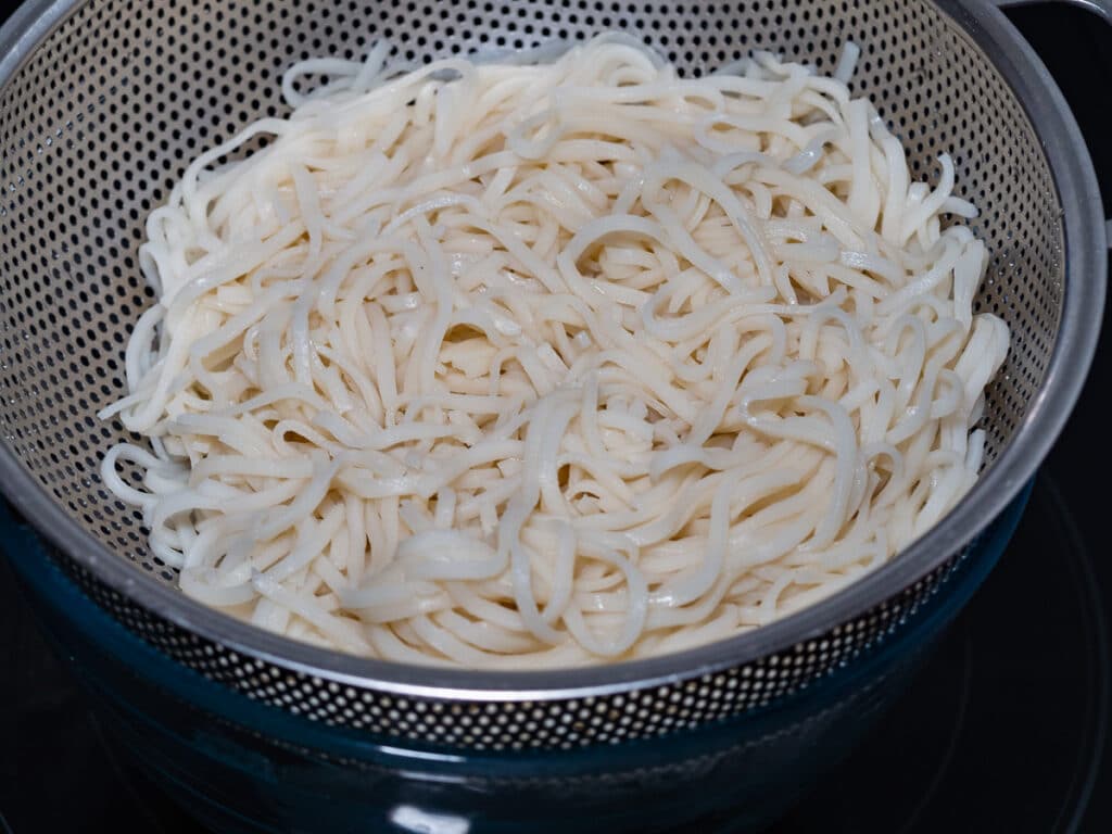 Soaked rice noodles in stainless steel strainer for chicken pho soup.