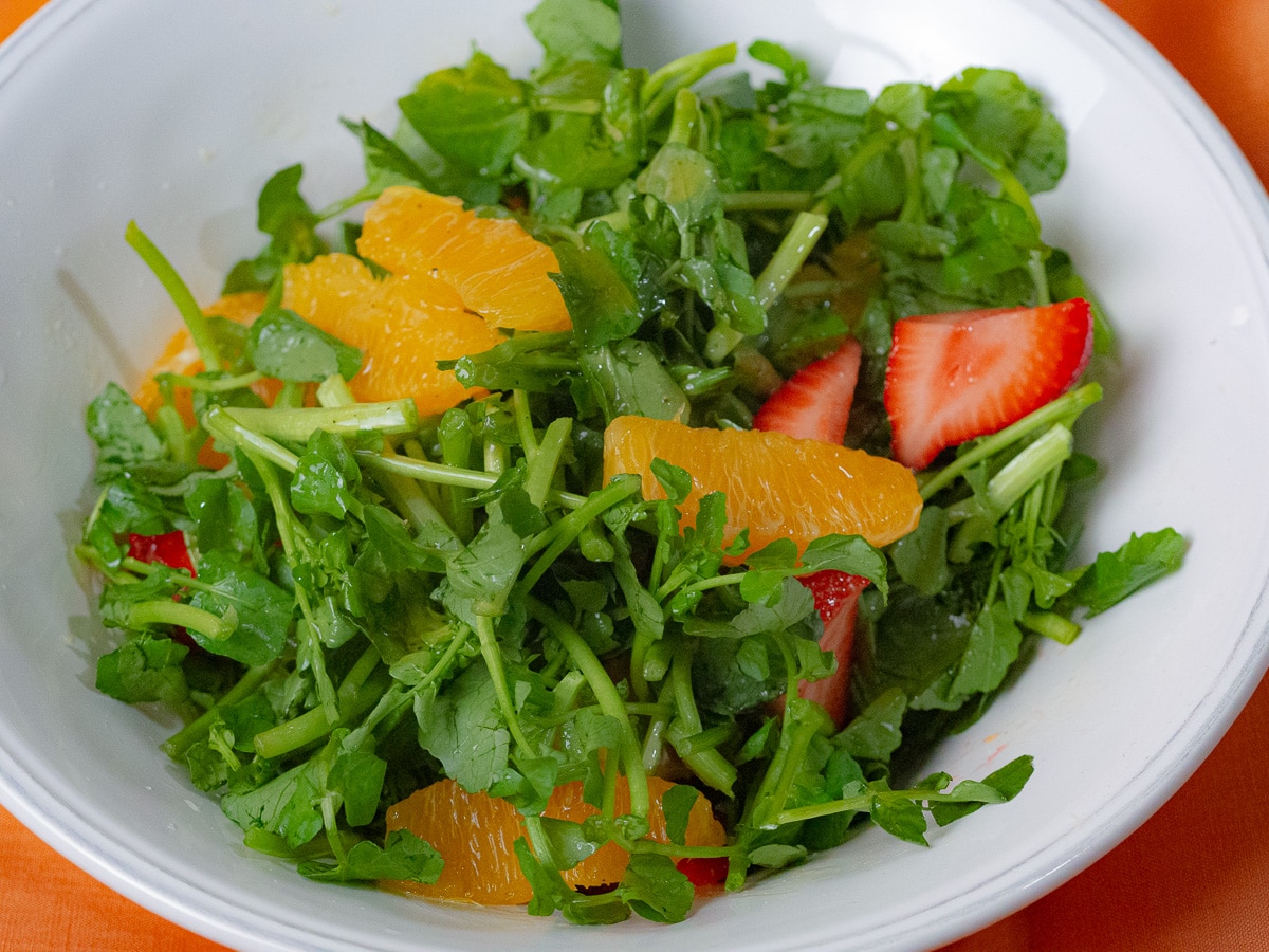 Watercress, section of oranges, sliced strawberries in a white serving bowl