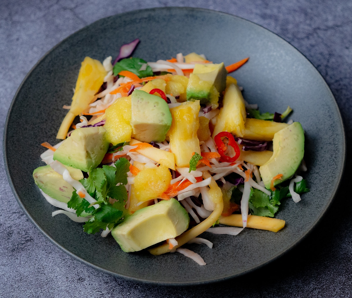Coleslaw with pineapple , avocado and chilli slices in a black salad bowl