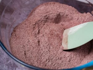 a mixture of chocolate cake dry ingredients in a glass mixing bowl with green spatula